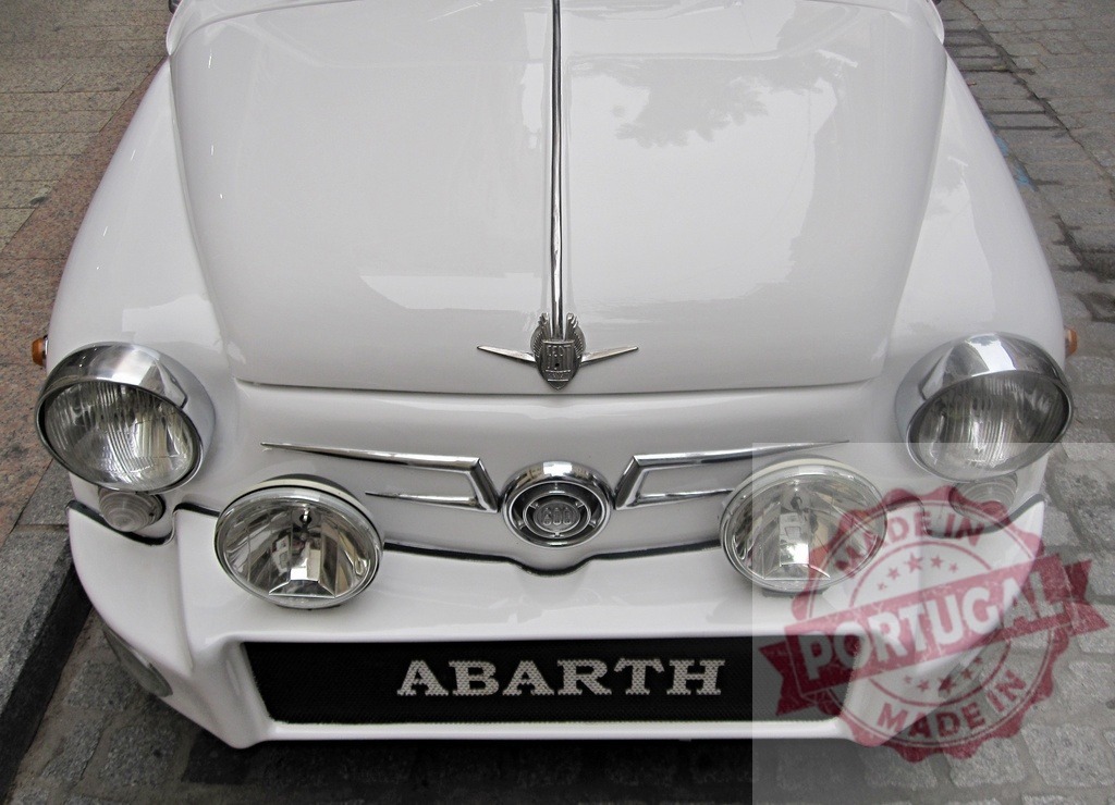 White Abarth 600 vintage car parked on a cobblestone street | Close-up of a white Abarth 600 vintage car parked on a cobblestone street, showcasing its iconic design and chrome details - Realized with Pictrs.com