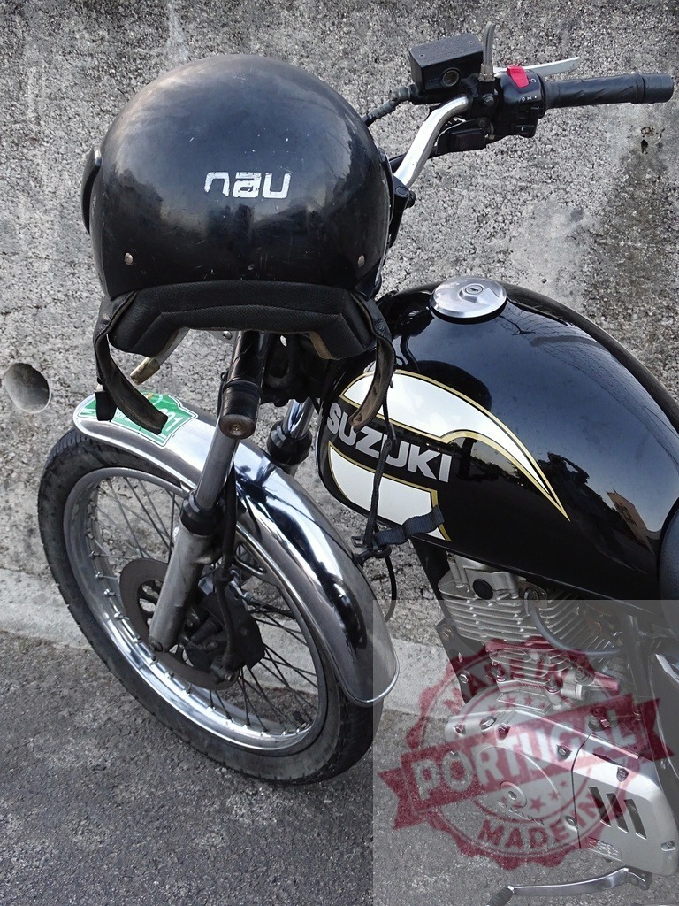 Black helmet resting on Suzuki motorcycle handlebar | Black helmet hanging on a parked Suzuki motorcycle's handlebar, ready for a safe ride - Realisiert mit Pictrs.com