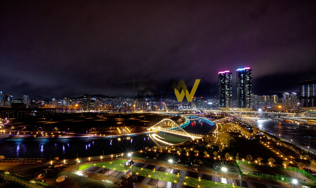 Hell und bunt beleuchteter Hafen in Busan-Skyline-Süd Korea | Das Bild zeigt die Geumgang-Fußgängerbrücke (Geumgang Pedestrian Bridge) bei Nacht in Sejong City, Südkorea. Die Brücke ist ein markantes Wahrzeichen von Sejong City und die erste zweistöckige Brücke in Korea. Sie ist 1.650 Meter lang und wurde 2021 fertiggestellt und im März 2022 für die Öffentlichkeit eröffnet. Ihr futuristisches Design wurde von der kreisförmigen Struktur der Stadt und der koreanischen Flagge inspiriert. Die obere Ebene ist für Fußgänger mit Ruhebereichen und Einrichtungen, während die untere Ebene ein Radweg ist.  - Realisiert mit Pictrs.com