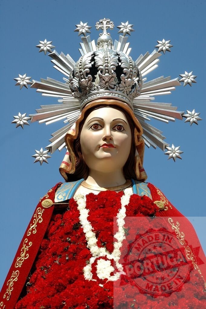 Virgin Mary religious statue crowned with halo and red flowers | Virgin Mary statue adorned with flowers, representing faith and Catholicism - Realized with Pictrs.com