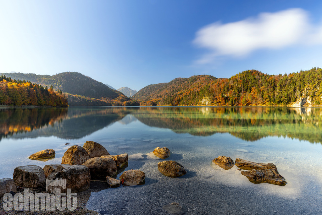 Wasserspiegelung am kleinen Alpsee bei Füssen im Allgäu | Herbstliche Wasserspiegelung am Kleinen Alpsee bei Füssen im Allgäu, umgeben von farbenprächtigen Wäldern und einer beeindruckenden Bergkulisse. Eine idyllische Aufnahme, die die besondere Stimmung eines herbstlichen Bergsees einfängt. - Realisiert mit Pictrs.com