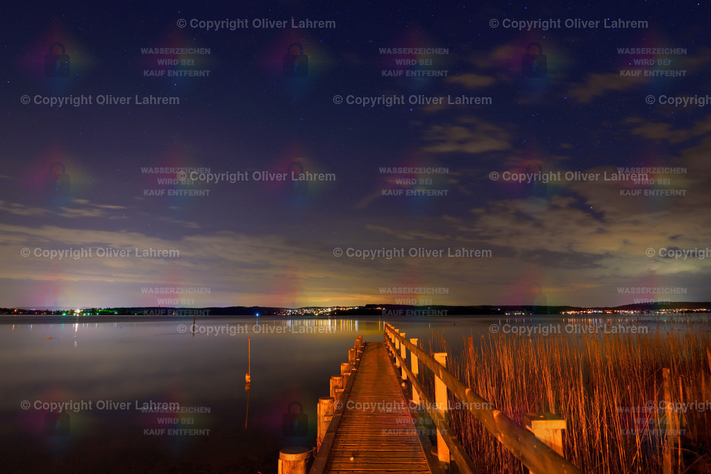 Bodensee in der Nacht | Sie Nacht ist über dem Bodensee und vom gegenüber liegenden Ufer sieht man die Lichter der Städt. Ein Bootssteg führt an Schliff vorbei zum Bodensee.