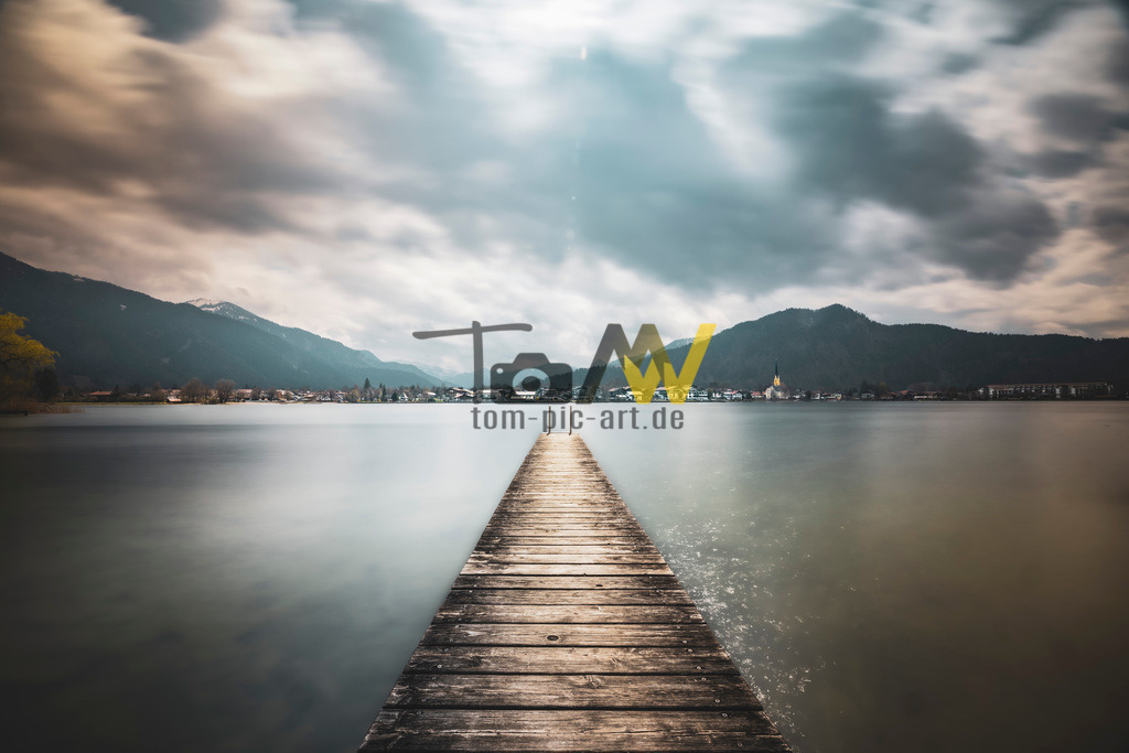 Klasse Bergpanorama mit langem Holz Steg---------Tegernsee  | Ein kleines Bergpanorma am Tegernsee , mit einem kleinen Steg davor. Dahinter die Ortschaft Rottach Egern.Das Bild zeigt den Tegernsee, einen beliebten Ausflugs- und Urlaubsort in Bayern, Deutschland. Der See liegt etwa 50 Kilometer südlich von München in den bayerischen Alpen. Er gehört zu den saubersten Seen Bayerns, was auf eine bereits in den 1960er Jahren geschaffene durchgängige Ringkanalisation zurückzuführen ist. Ansehnliche Berge, wie der 1722 Meter hohe Wallberg, umrahmen den See. Das Ufer ist fast vollständig öffentlich zugänglich, was ihn zu einem beliebten Ziel für Spaziergänge und Radtouren macht.  - Realisiert mit Pictrs.com