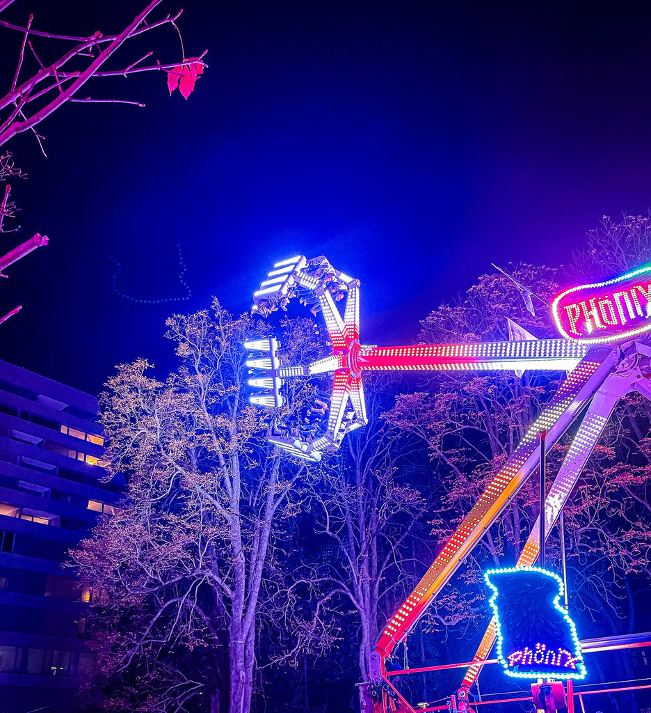 Wandbild Kunstdruck Poster – Basel & Region: Phönix-Ride in Neon Lights auf der Basler Herbstmesse von Robert Steinke | Ein spektakuläres, dynamisches Kunstwerk der modernen Night-Photography, das die pure Energie und Magie der traditionsreichen Basler Herbstmesse einfängt. Diese detailreiche Aufnahme zeigt das Fahrgeschäft „Phönix“ in voller Fahrt vor dem tiefblauen Nachtshimmel. Das atemberaubende Zusammenspiel aus leuchtenden Neon-Farben in Pink, Violett und hellem Weiß erzeugt durch die Bewegungsunschärfe faszinierende Lichtspuren, die sich messerscharf von der Dunkelheit abheben. Die von den Lichtern bunt angestrahlten Bäume im Hintergrund verleihen der Szenerie eine fast surreale, elektrisierende Atmosphäre.Dieses ausdrucksstarke Motiv bringt pure Dynamik, urbane Lebendigkeit und ein modernes Nightlife-Gefühl in deine Räume. Ein absolut spektakulärer Blickfang für ein modernes Wohnzimmer, das kreative Büro, ein helles Loft oder für jeden echten Basel-Fan, der die unvergleichliche Energie der Herbstmesse liebt.Um die leuchtenden Neon-Farben und die knackigen Kontraste der Nacht perfekt zur Geltung zu bringen, empfehle ich den Druck auf unseren Premium-Materialien: Erlebe maximale Tiefenwirkung und kinoreife Farbbrillanz auf edlem Acrylglas oder eine moderne, cleane Galerie-Eleganz auf robustem Alu-Dibond. Hol dir die Magie der Basler Nacht direkt an deine Wand! - Realisiert mit Pictrs.com