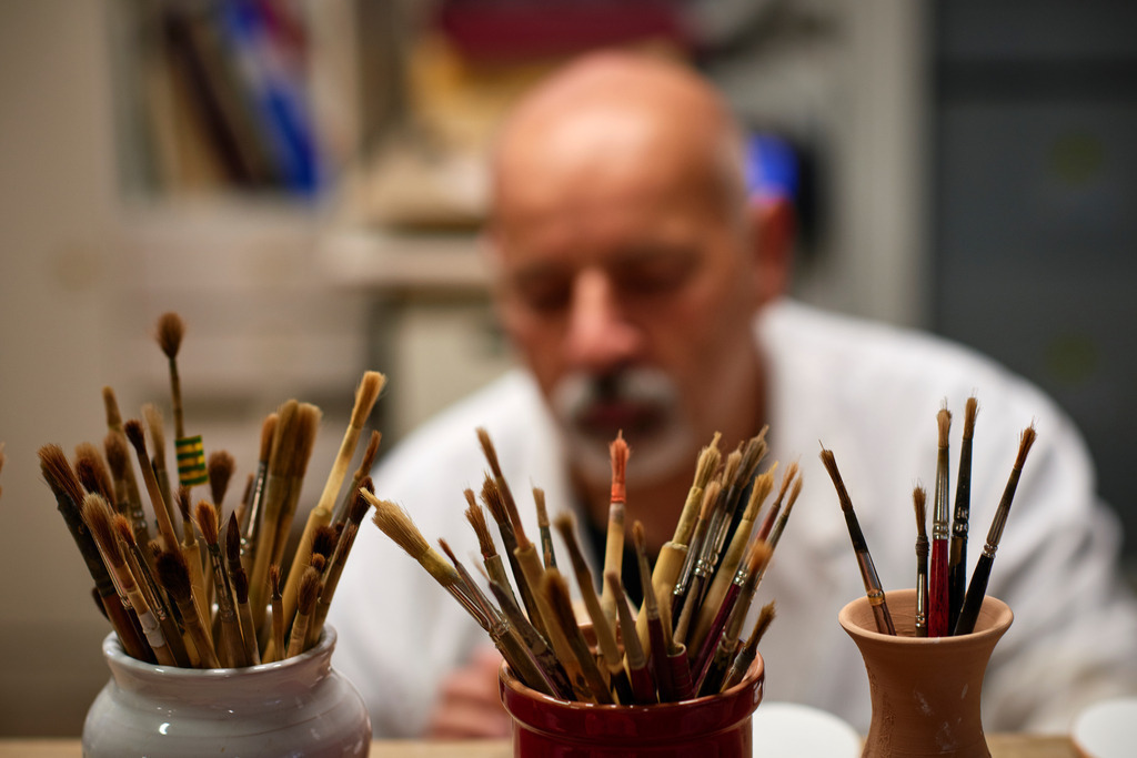 Maestro Caravaggi beim bemalen des Tellers | Deruta, Italien - August 31, 2016: Keramikmanufaktur Torretti; Maestro Caravaggi beim bemalen eines Tellers, im Vordergrund mehrere Pinsel. - Realisiert mit Pictrs.com