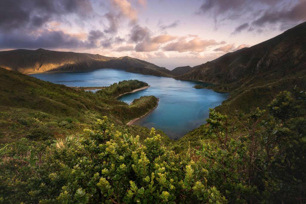 Feuersee – Lagoa do Fogo auf São Miguel | Hoch oben in den Bergen von São Miguel liegt der Lagoa do Fogo – ein Kratersee wie aus einer anderen Welt. Umgeben von dichtem Grün und steilen Hängen entfaltet sich hier ein stilles Naturparadies. Das warme Licht des späten Tages lässt das Wasser tiefblau leuchten und verleiht der Landschaft eine fast mystische Stimmung. Ein Ort, der dem Namen „Feuersee“ alle Ehre macht. - Realisiert mit Pictrs.com