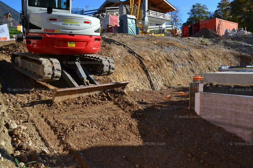 Keller hinterfüllen | Bagger mit Planierschild neben hinterfülltem Baukörper