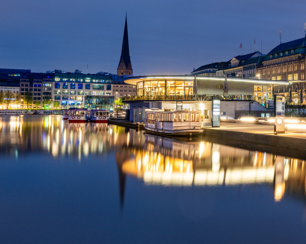 Hamburger Binnenalster zur blauen Stunde | Die beleuchteten Gebäude der Hamburger Innenstadt spiegeln sich zur blauen Stunde im ruhigen Wasser der Binnenalster. Die tiefblaue Abendstimmung verleiht der klassischen Stadtkulisse eine besonders elegante Wirkung. - Realisiert mit Pictrs.com
