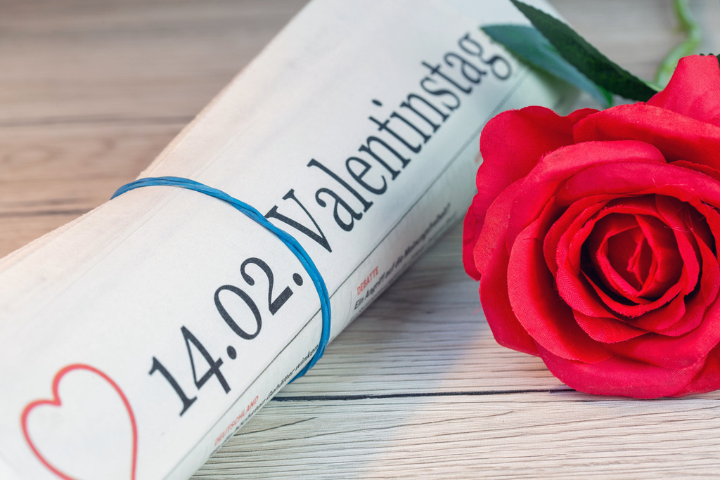 Am 14.02. ist Valentinstag | Symbolische Zeitung mit dem Titel 14.02. VALENTINSTAG neben einer roten Rose - Realisiert mit Pictrs.com