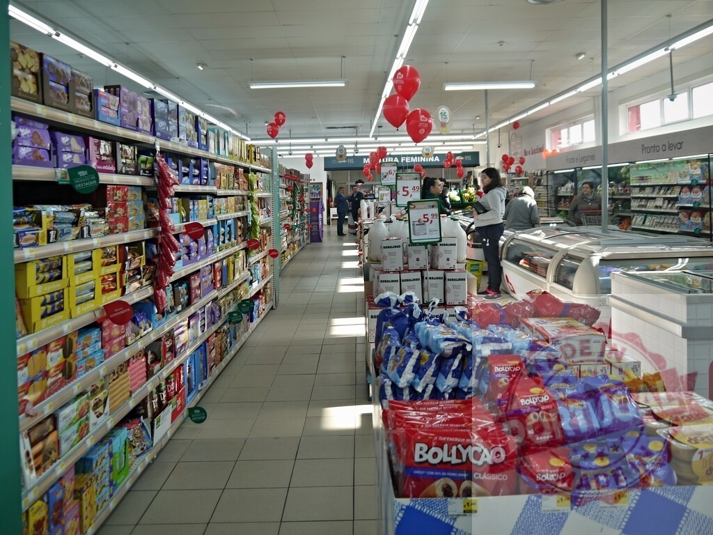 Supermarket aisle distributing various grocery products to shoppers | Supermarket aisle filled with shelves of products and customers shopping for groceries under red balloons - Realized with Pictrs.com