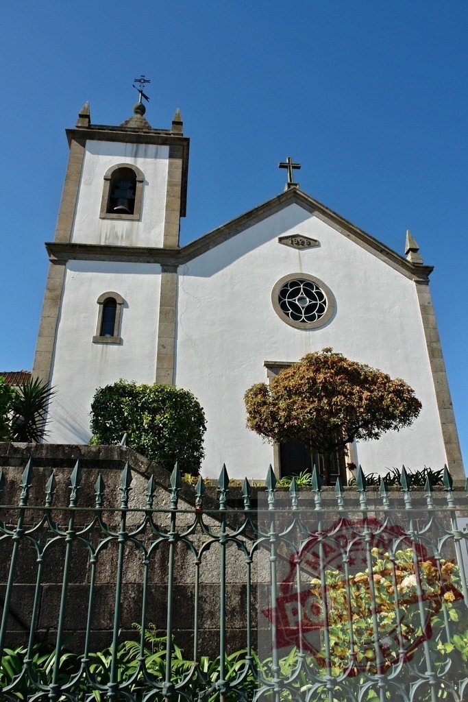 White church building with bell tower and cross. Region Norte - Portugal | White church building with a bell tower and cross standing under a clear blue sky - Realized with Pictrs.com