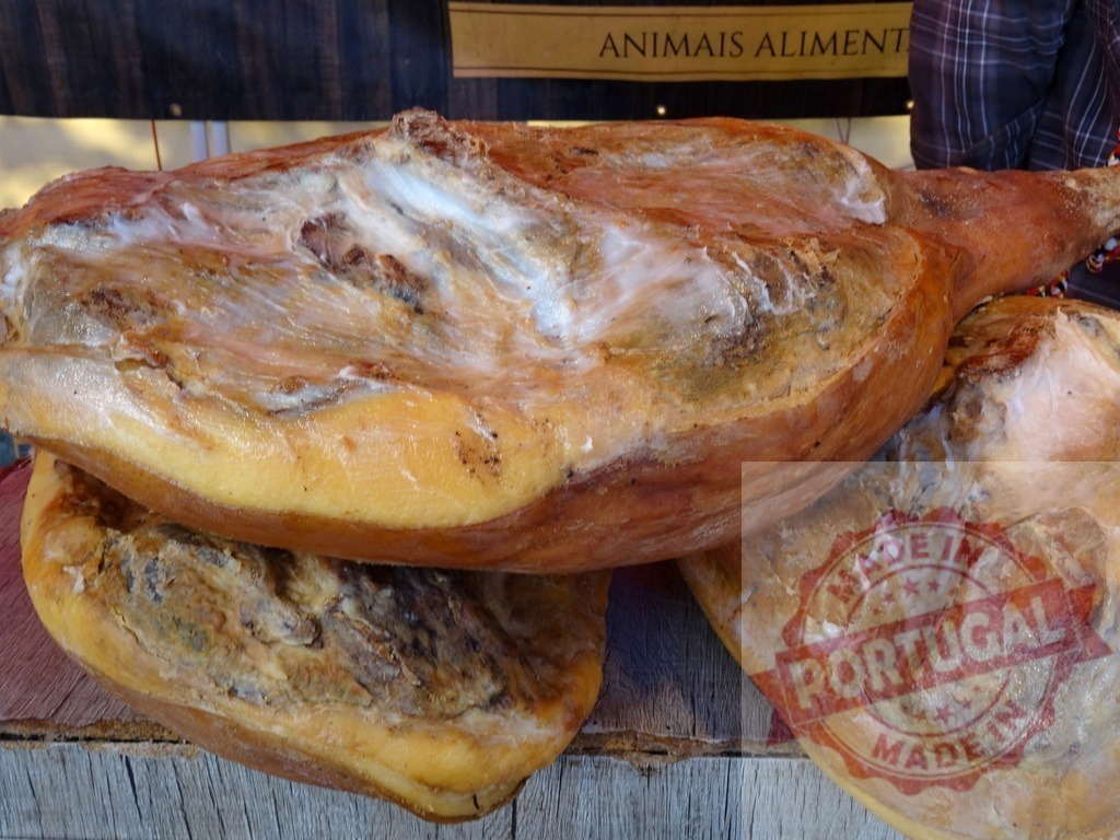 Traditional dry-cured ham legs at market stall | Pork legs curing, showcasing a rustic, traditional food preparation - Realisiert mit Pictrs.com