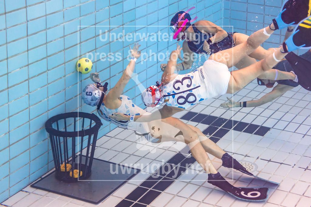 24. - 26.11.2023: Unterwasser-Rugby Champions Cup 2023  | Damen-Spiel: NJ Hammerheads (USA) in blau gegen Barcelona (Spanien) in weiß. Die amerikanische Meisterin Julia Gomez (blau #28) versucht den Ball, über die spanische Torwärtin Aida Peiro (weiß #6), in das offene Tor zu stoßen.  Giovanna Bautista (weiß #83) eilt zur Hilfe um den Ball abzufangen. - Realisiert mit Pictrs.com