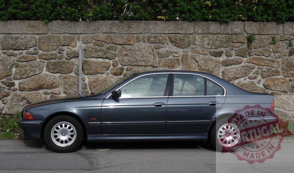 BMW E39 5 Series sedan parked by stone wall | BMW 5 Series E39 model sedan parked next to a rustic stone wall with green foliage above - Realisiert mit Pictrs.com