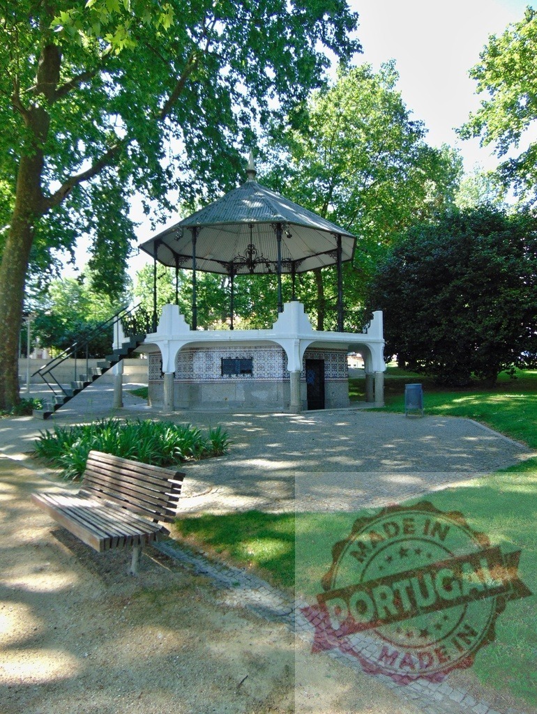 Bandstand in park with bench and green trees. Portugal - Norte | Park bandstand with decorative tiles, surrounded by a wooden bench, gravel, and grass on a sunny day - Realized with Pictrs.com