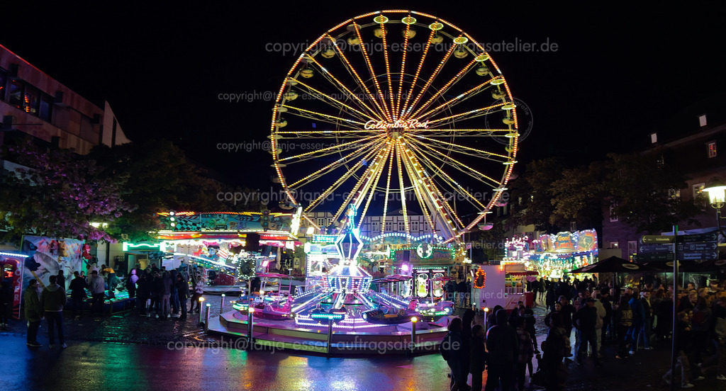 Kirmes in Brilon bei Nacht | Brilon, North Rhine Westphalia/Germany - September 23rd, 2023: Beleuchtetes Riesenrad und Kinderkarussell abends auf der Briloner Kirmes. Unbekannte Besucher schlendern vorbei.