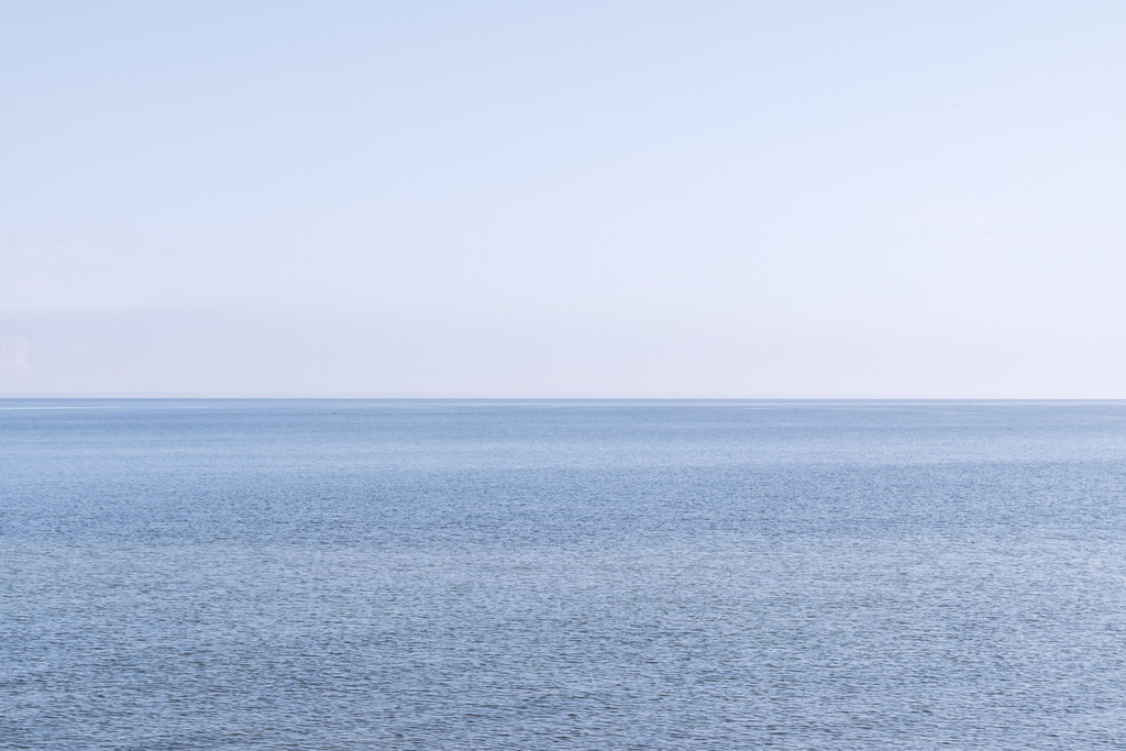 Endlose Ostsee - Minimalistischer Blick über das Meer | Dieses hochgradig minimalistische Wandbild fängt die zeitlose Stille und unendliche Weite der Ostsee vor Falshöft ein. Die klare Teilung von sanft bewegter Meeresoberfläche und lichtem Himmel schafft einen Ort der visuellen Ruhe und Entschleunigung. Mit seinen dezenten Blautönen fügt sich dieses Kunstwerk elegant in moderne, anspruchsvolle Raumkonzepte ein und bringt ein Gefühl von tiefer Gelassenheit an jede Wand.