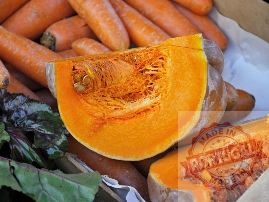 Fresh pumpkin slice with carrots and greens in market | Pumpkin slice revealing seeds and fibers among fresh carrots and leafy greens - Realized with Pictrs.com