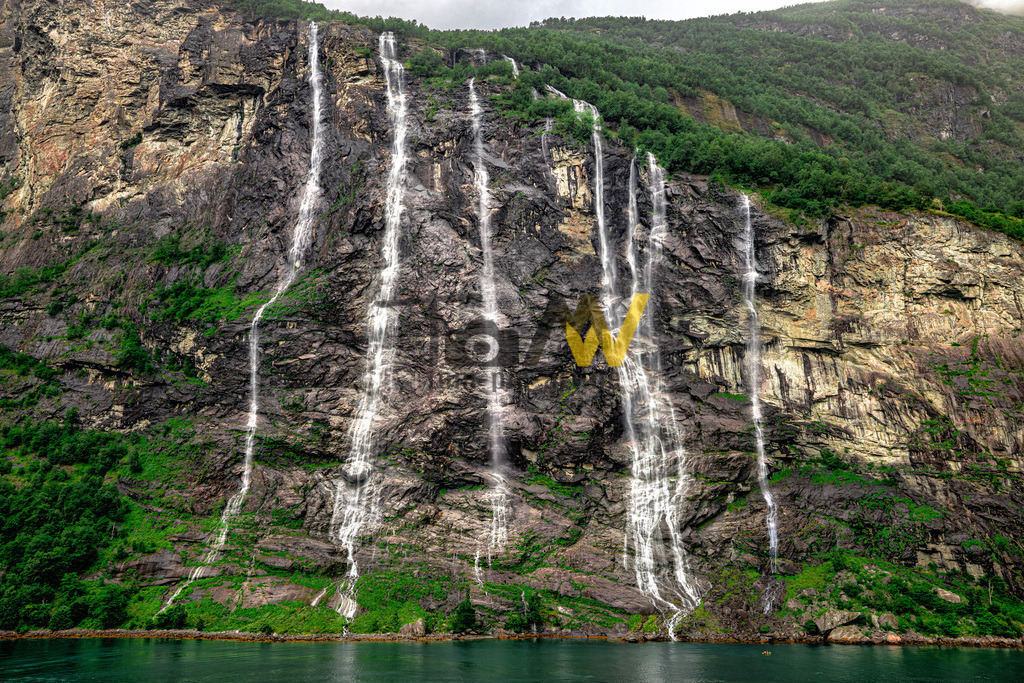 Die Wasserfälle im Geirangerfjord-Die 7 Schwestern-Norwegen | Das Bild zeigt die "Sieben Schwestern" (norwegisch: De syv søstrene), einen berühmten Wasserfall im Geirangerfjord in Norwegen. Der Wasserfall besteht aus sieben separaten Strömen, die direkt nebeneinander vom Berg in den Fjord stürzen. Die Gesamthöhe beträgt etwa 410 Meter, wobei der höchste freie Fall etwa 250 Meter misst. Die Wasserfälle sind besonders während der Schneeschmelze im Frühjahr und Sommer spektakulär. Einer Sage nach repräsentieren die sieben Ströme unverheiratete Schwestern, während ein gegenüberliegender Wasserfall, der "Freier", erfolglos um ihre Hand anhält.  - Realisiert mit Pictrs.com