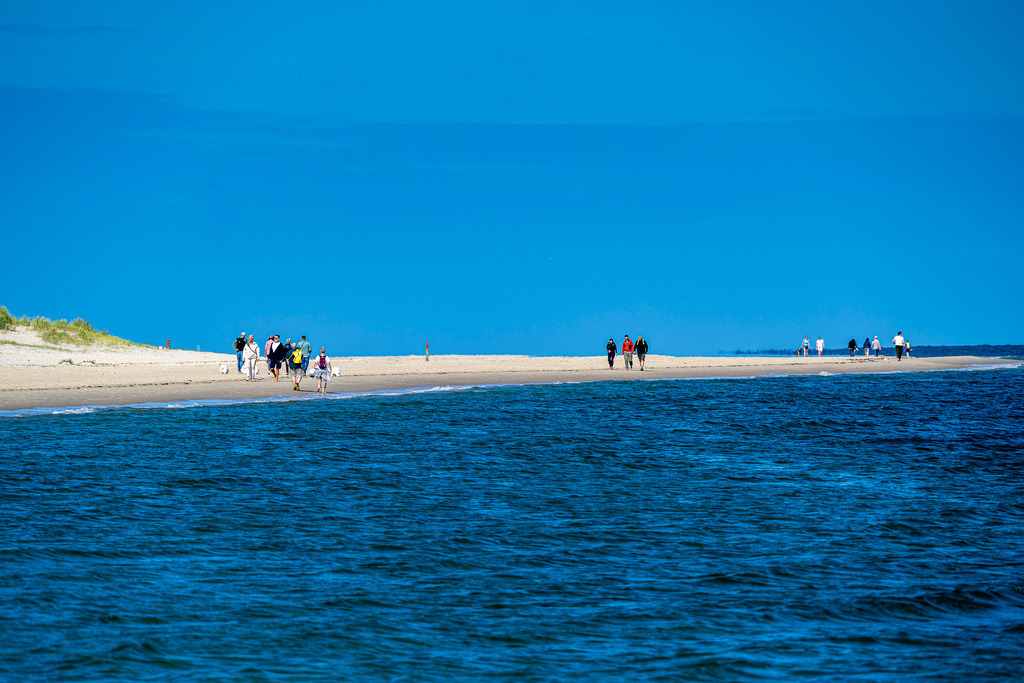 Spaziergänger am Sandstrand der Westfriesischen Insel Texel bei strahlendem Sonnenschein | Eine Gruppe von Urlaubern und Spaziergängern flaniert an einem sonnigen Tag entlang einer weitläufigen Sandbank auf der niederländischen Nordseeinsel Texel. Die Aufnahme zeigt die charakteristische Küstenlandschaft mit feinem Sandstrand, sanftem Wellengang des tiefblauen Meeres und klarem, blauem Himmel. Das Motiv eignet sich ideal für redaktionelle Beiträge zu den Themen Tourismus, Inselurlaub in den Niederlanden, Nordsee, Sommerurlaub, Erholung sowie Natur- und Küstenschutz. - Realisiert mit Pictrs.com