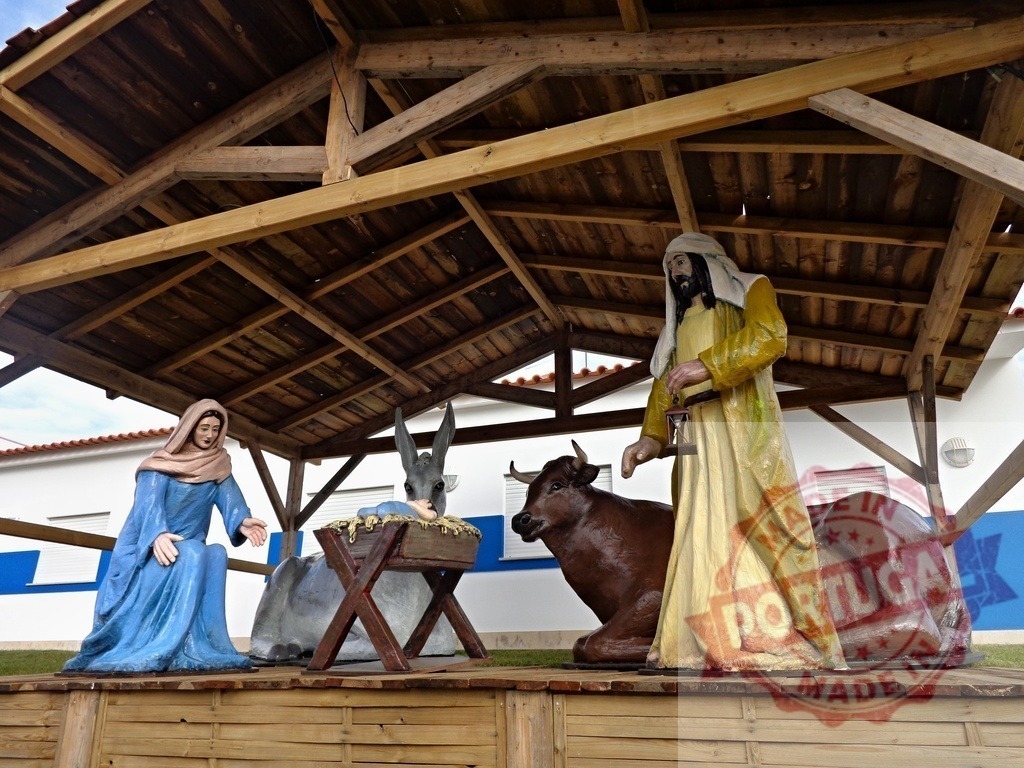 Nativity scene representing the birth of Jesus with Mary, Joseph, ox and donkey under a wooden shelter | Outdoor christmas nativity scene with colorful statues of the holy family, ox and donkey under a wooden shelter - Realized with Pictrs.com