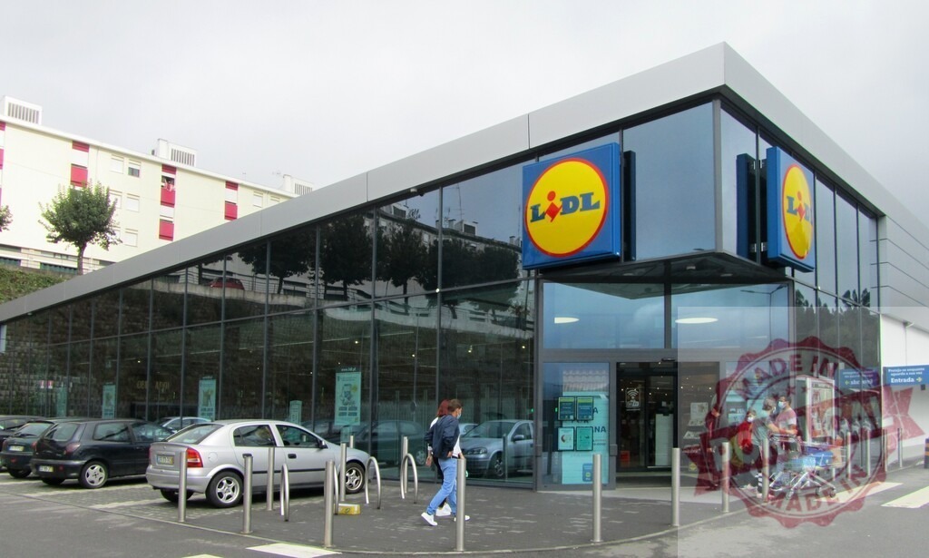 Lidl supermarket exterior with customers entering and parking lot | Customers entering a modern Lidl supermarket building with a parking lot and glass facade - Realisiert mit Pictrs.com