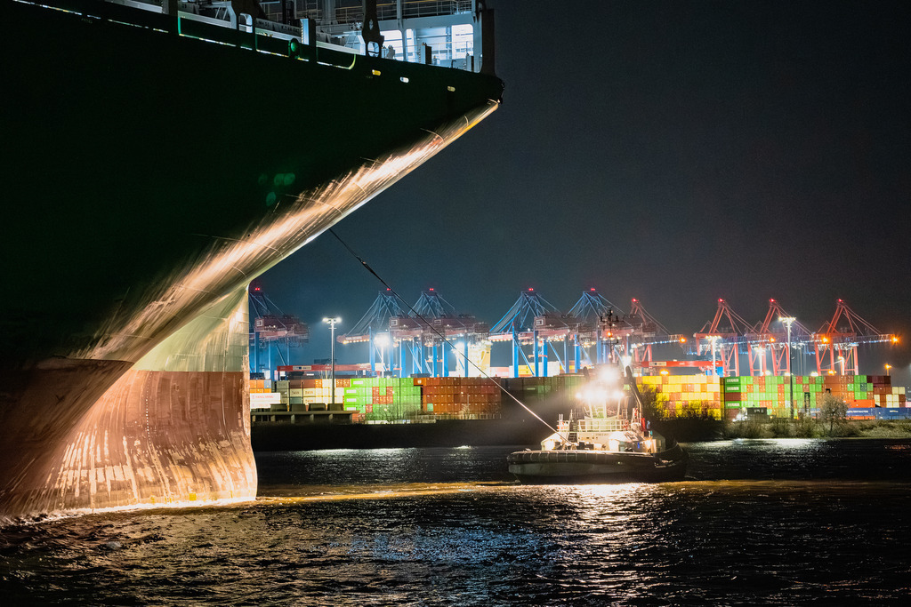 Kraftpaket im Scheinwerferlicht | Der Assistenzschlepper VB Mercury im Einsatz am Bug des 400-Meter-Containerschiffs Ever Act. Die Aufnahme zeigt das Manöver unter der Beleuchtung eines Containerterminals im Hamburger Hafen.  - Realisiert mit Pictrs.com
