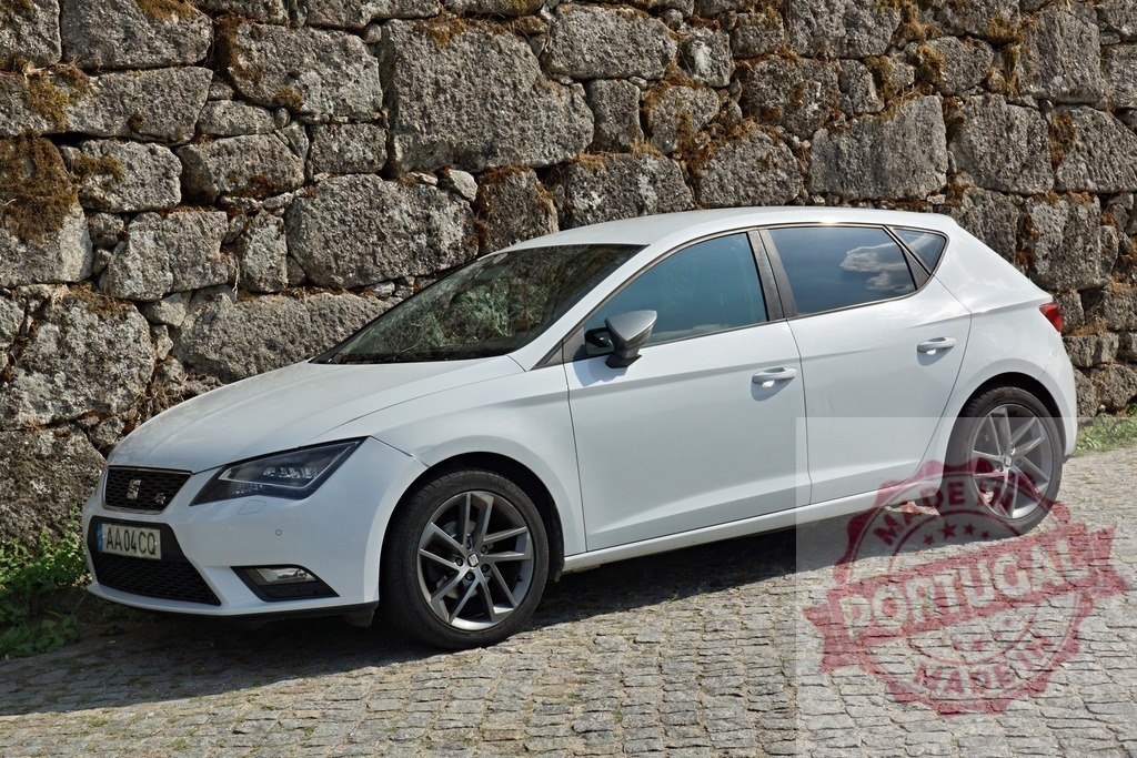 White Seat Leon hatchback parked on cobblestone street | White Seat Leon hatchback parked next to a stone wall on a cobblestone street - Realized with Pictrs.com