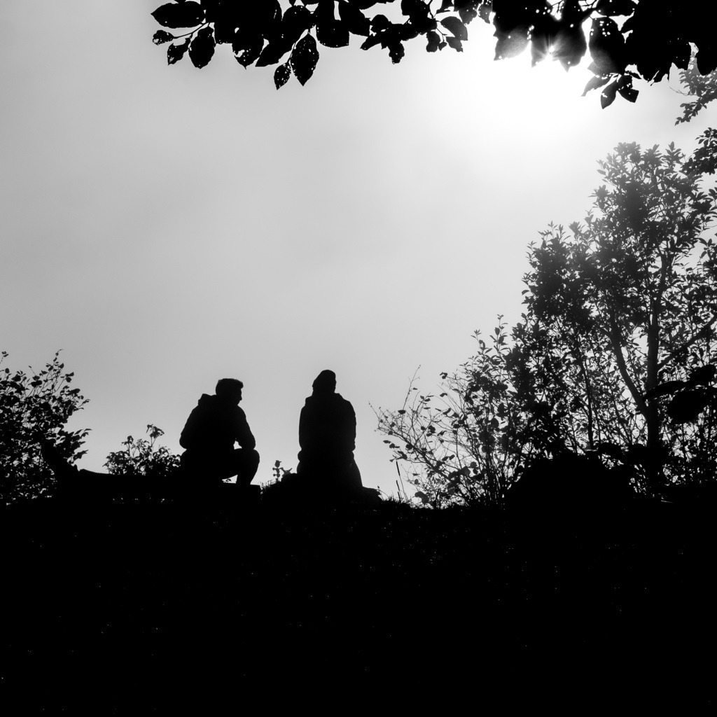 Ausruhen bevor es weitergeht | Bild ist umrahmt von Ästen und zwei Personen sitzen auf Steinen und ruhen sich aus. - Realisiert mit Pictrs.com