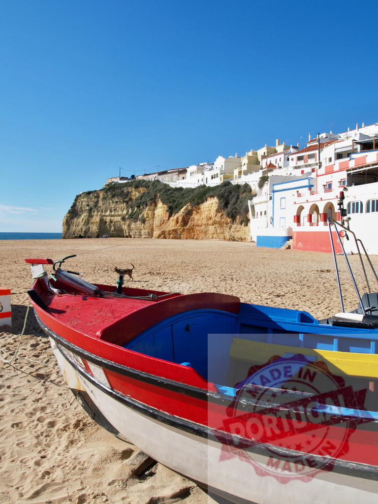 Colorful fishing boat on Carvoeiro beach, Portugal | Fishing boat resting on sand with coastal town and cliffs under blue sky - Realisiert mit Pictrs.com