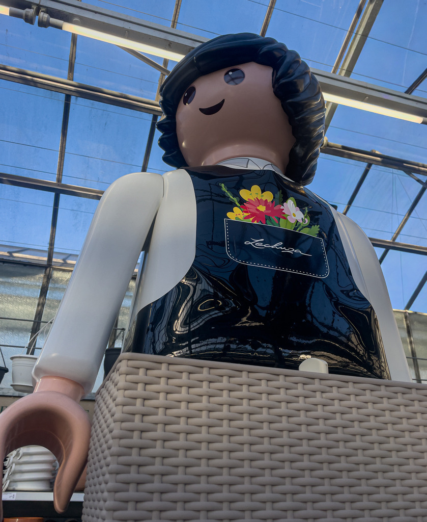 Basel Botanischer Garten – Übergroßer Playmobil Gärtner Kunst Wandbild | Kreative und surreale Fotokunst aus Basel: Dieses High-End Wandbild zeigt eine detailreiche Nahaufnahme einer übergroßen Playmobil-Gärtnerfigur vor einer modernen, lichtdurchfluteten Gewächshaus-Architektur. Das harmonische Zusammenspiel aus nostalgischer Kindheitserinnerung und modernem, urbanem Design macht dieses Werk zu einem einzigartigen Blickfang. Perfekt in Galeriequalität auf Acrylglas oder Alu-Dibond für Wohnräume, Büros oder kreative Arbeitsplatz-Konzepte. - Realisiert mit Pictrs.com