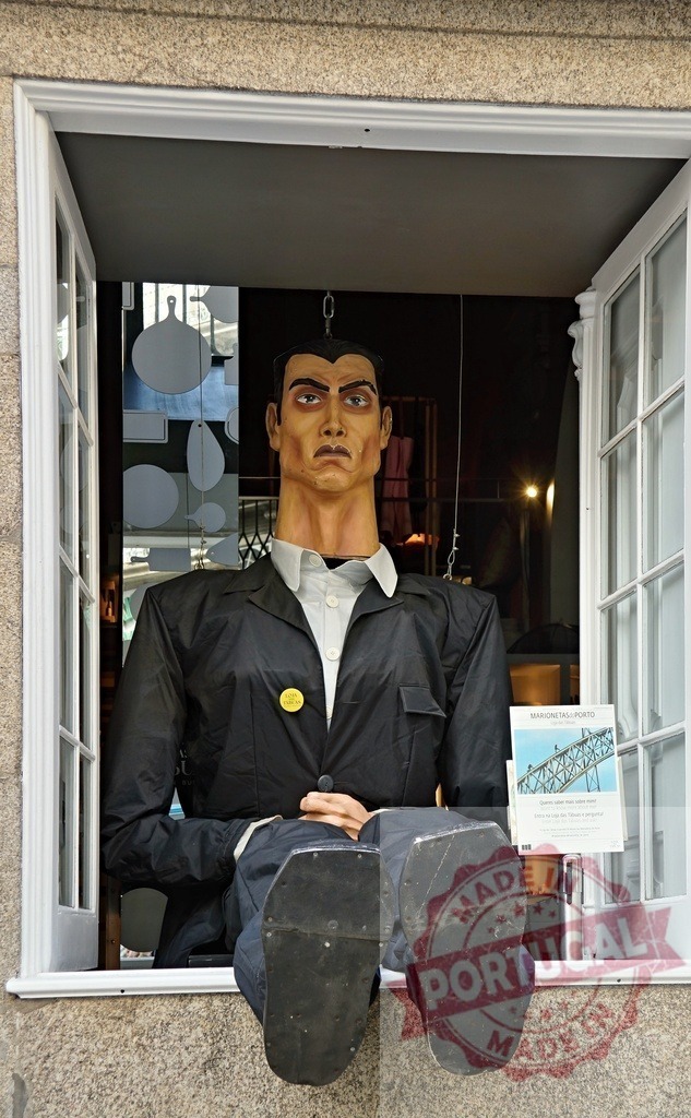 Giant marionette puppet figure sitting in window in Porto | Giant marionette figure with a black suit observing from an open window - Realized with Pictrs.com