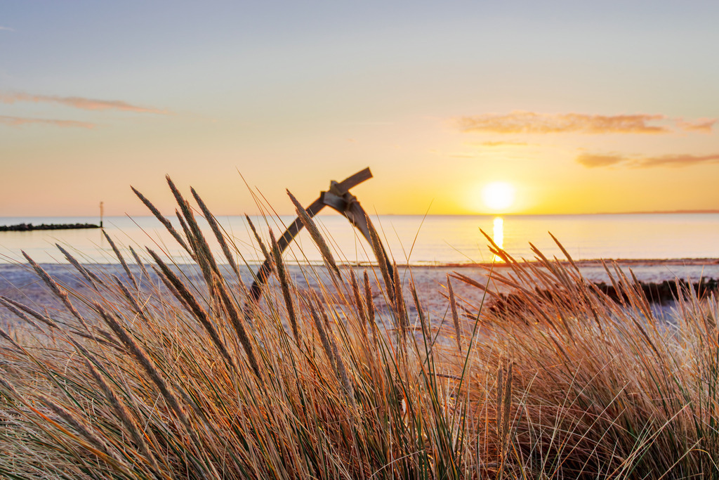 Wandbild: Magischer Sonnenaufgang am Strand in Damp | Sanfte Farben, beruhigende Naturmotive und die friedliche Weite des Meeres – dieses Wandbild strahlt Harmonie und Entspannung aus. Die aufgehende Sonne über der Ostsee taucht den Himmel in warmes Orange, während sich der Strandhafer sanft im Morgenlicht bewegt. Mit seinem weichen Farbspiel und der maritimen Ruhe fördert das Bild das Wohlbefinden und schafft eine angenehme Raumwirkung. - Realisiert mit Pictrs.com