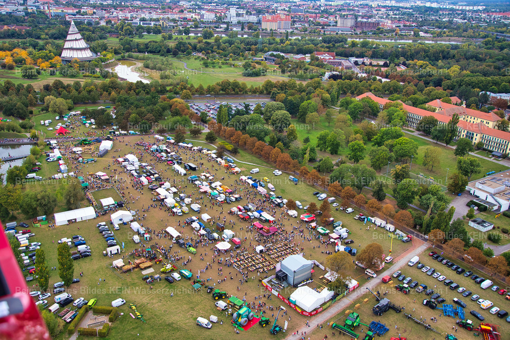 erntedankfest_magdeburg_9575 | Diese Luftaufnahme zeigt das weitläufige Gelände des Erntedankfestes im Elbauenpark während eines sonnigen Herbsttages. Die zahlreichen Ausstellerflächen, Präsentationsstände und Aktionsbereiche sind übersichtlich angeordnet und vermitteln aus der Luft einen eindrucksvollen Überblick über die Größe und Organisation der Veranstaltung. Die herbstlichen Farben des Elbauenparks schaffen dabei eine stimmungsvolle Kulisse für eines der beliebtesten Feste Sachsen-Anhalts.Die Aufnahme entstand im Auftrag der Agrarmarketinggesellschaft Sachsen-Anhalt, um die Veranstaltung aus der Luft zu dokumentieren. Erst aus dieser Perspektive werden die sorgfältige Planung, die Vielfalt der Aussteller und die Dimension des Festgeländes sichtbar. Luftbilder leisten dabei einen wertvollen Beitrag zur Dokumentation großer Veranstaltungen und eröffnen Blickwinkel, die Besuchern vom Boden aus verborgen bleiben.Das Erntedankfest verbindet seit vielen Jahren Landwirtschaft, regionale Produkte und Tradition mit einem abwechslungsreichen Familienprogramm. Die Luftaufnahme hält nicht nur die besondere Atmosphäre des Festes fest, sondern dokumentiert zugleich einen wichtigen Treffpunkt für Erzeuger, Unternehmen und Besucher aus ganz Sachsen-Anhalt. - Realisiert mit Pictrs.com