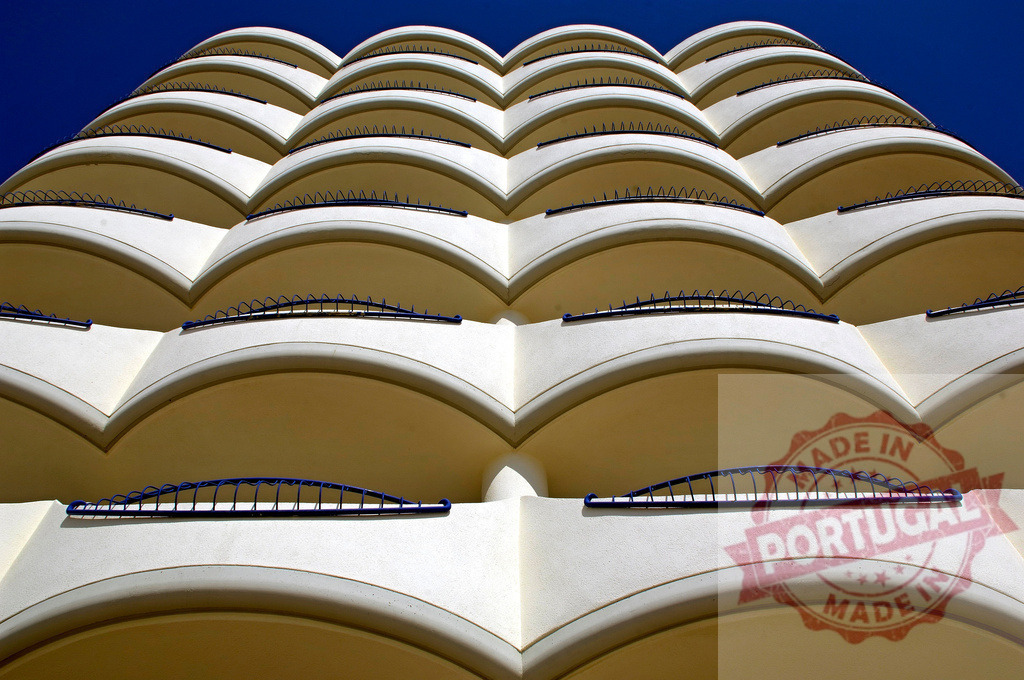 Building facade showing abstract curved balconies under blue sky. Espana - Cadiz | Modern architectural repetitive pattern with curved balconies and blue sky background - Realisiert mit Pictrs.com