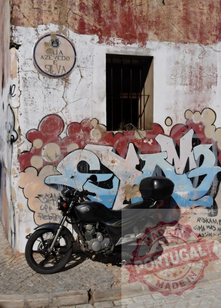 Motorcycle parked against a graffiti street art wall in Lisbon | Motorcycle parked on a cobbled street in Lisbon with a weathered wall displaying graffiti art - Realized with Pictrs.com