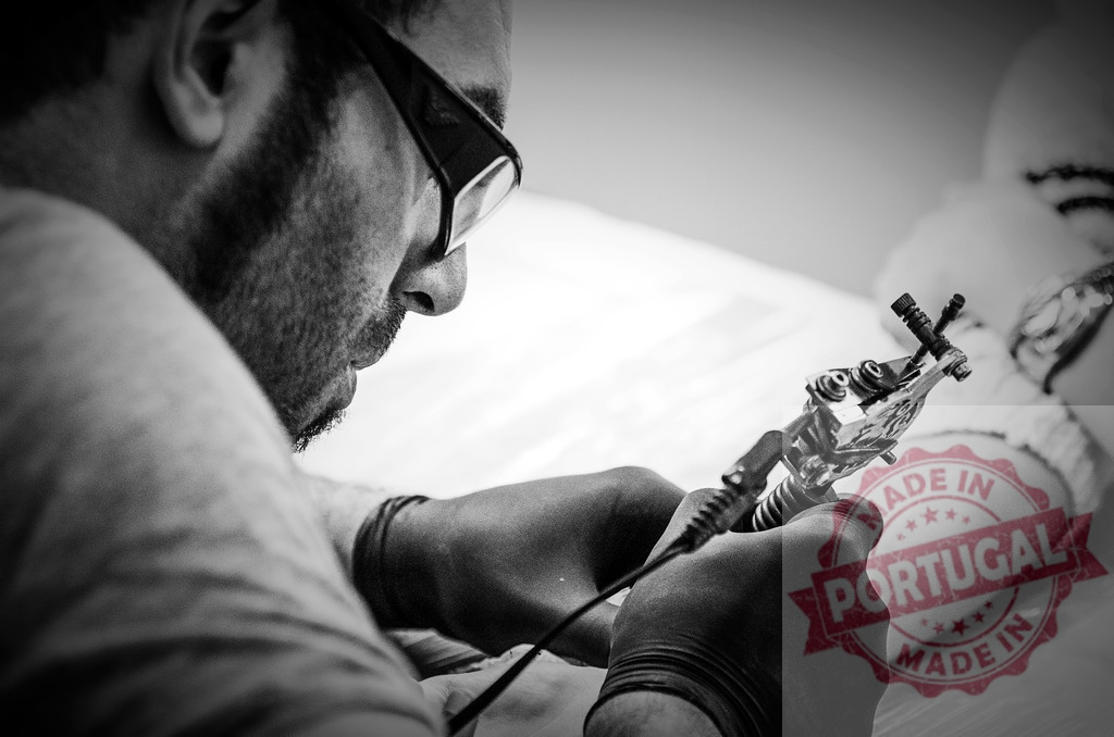 Tattoo artist wearing gloves and glasses carefully drawing a tattoo on a client's arm | Tattoo artist concentrating on his work, carefully drawing a tattoo with a tattoo machine - Realized with Pictrs.com