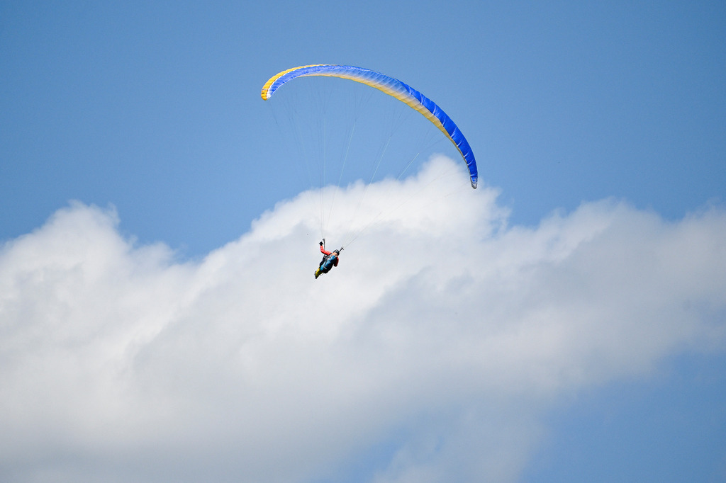 Dem Himmel so nah: Der Traum vom Fliegen | Ein Moment purer Schwerelosigkeit und unendlicher Weite: Ein Gleitschirmflieger zieht mit seinem leuchtend blau-gelben Schirm einsame Kreise hoch über den Dingen. Unter ihm die Welt, vor ihm die grenzenlose Freiheit des Himmels. Wie ein bunter Farbtupfer hebt er sich von den weichen, strahlend weißen Sommerwolken ab, die sanft durch das tiefe Himmelsblau ziehen. Diese Aufnahme fängt das berauschende Gefühl von Freiheit, den Mut zum Abenteuer und die tiefe Sehnsucht ein, den Alltag hinter sich zu lassen und einfach dem Wind zu folgen. - Realisiert mit Pictrs.com