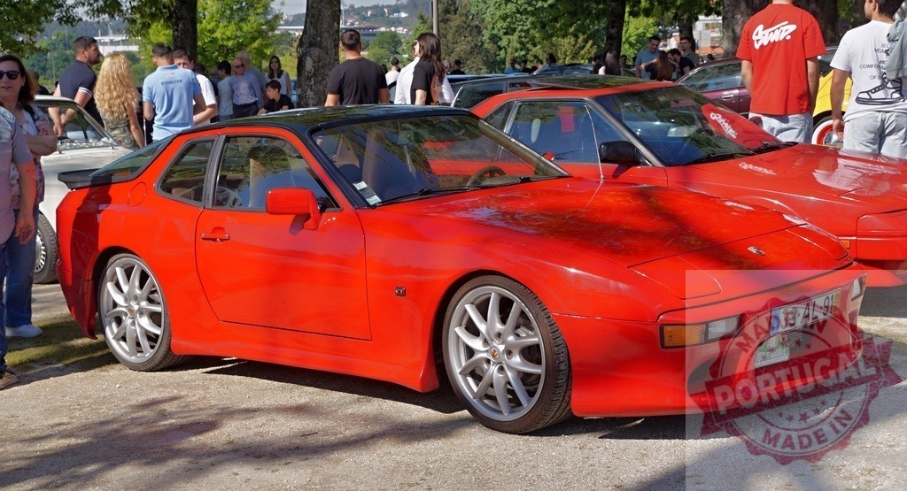 Red Porsche 944 sports car standing at classic car show | Classic red Porsche 944 coupe attracting attention at an outdoor car meet - Realized with Pictrs.com