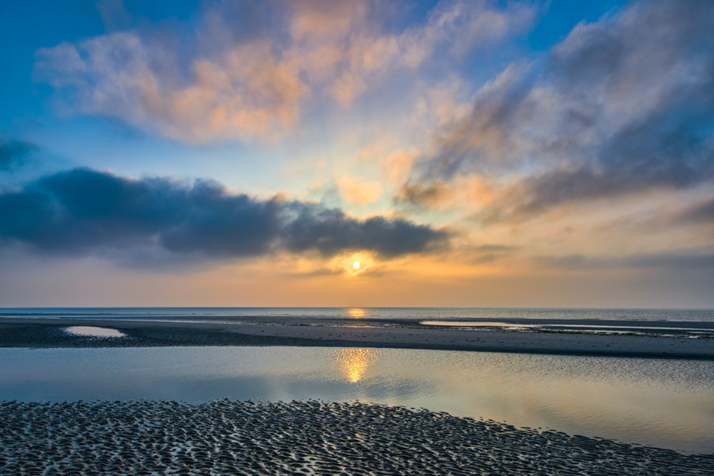 Sonnenuntergang St. Peter-Ording | Bei Ebbe im Wattenmeer geht die Sonne umrahmt von Wolken unter, an der Nordseeküste vor St. Peter-Ording. — Auflösung des Originals: 6015 x 4010 px. - Realisiert mit Pictrs.com
