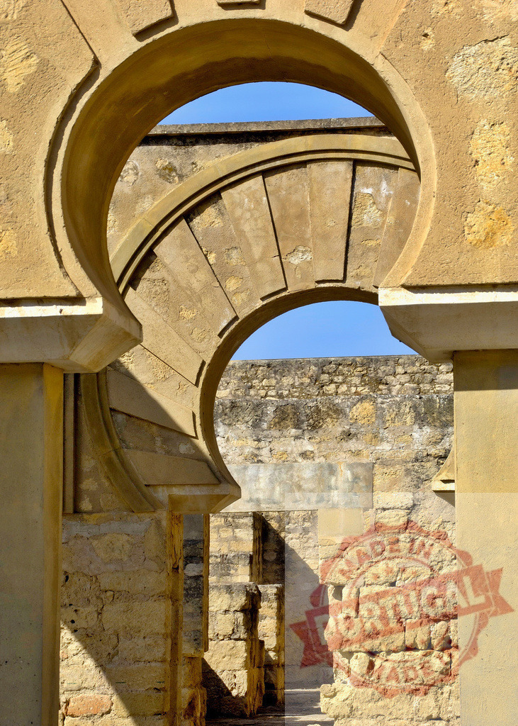 Medina Azahara horseshoe arch framing ancient ruins in Cordoba. Spain - Cordoba | Ancient Moorish architecture and ruins of Medina Azahara under a clear blue sky - Realized with Pictrs.com
