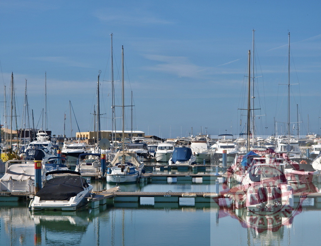 Many boats docked in a busy marina under blue sky | Boats and yachts moored in a tranquil harbor with clear reflections on the water - Realized with Pictrs.com