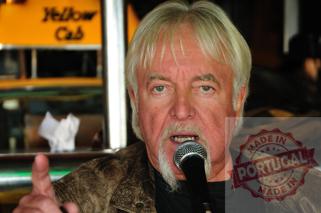 Older musician singing into microphone performing live | Older man with white hair and goatee singing into a microphone, gesturing with his hand - Realized with Pictrs.com