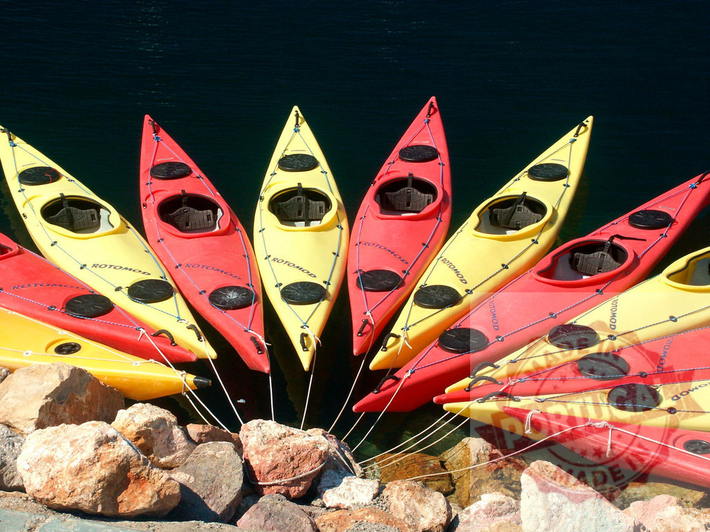 Colorful kayaks resting on a rocky shore, ready for paddling adventure | Red and yellow kayaks arranged on the shore, inviting adventurers to explore the waters - Realisiert mit Pictrs.com