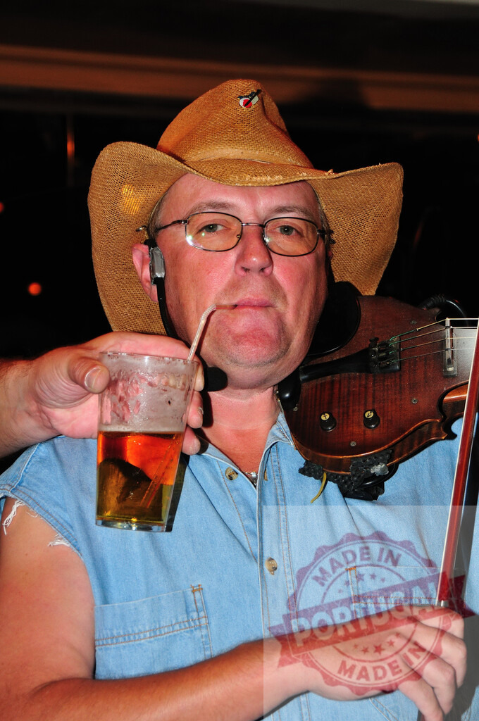 Cowboy musician playing violin and drinking beer | Man in cowboy hat performing country music, holding a fiddle and drinking beer with a straw - Realized with Pictrs.com