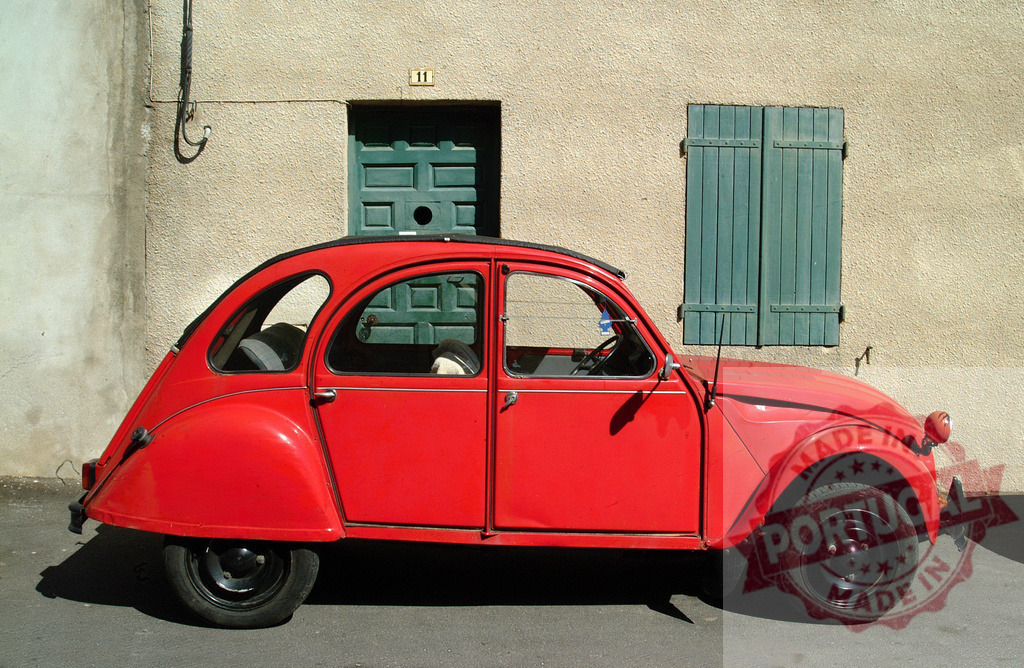 Red Citroën 2CV parked in front of a house with green shutters and door | Classic red Citroën 2CV parked on a sunny day, adding a touch of vintage charm to a picturesque street - Realisiert mit Pictrs.com