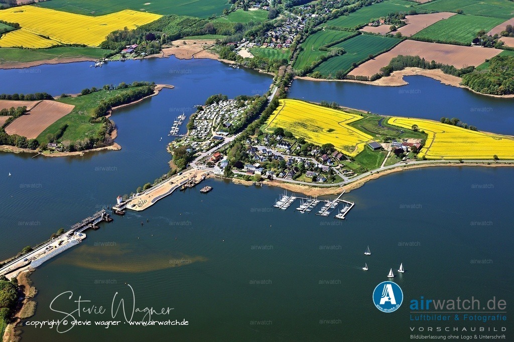 Luftbild Ostseefjord Schlei, Boren-Lindaunis Schleibrücke, Campingplatz Lindaunis, Sportboothafen Lindaunis | Sportboothafen Lindaunis ist ein idyllisch gelegener Yachthafen direkt an der Schlei in Schleswig-Holstein, bekannt als „Wo die Schlei am schönsten ist“. Der familiär geführte Hafen bietet 98 Sommerliegeplätze mit bis zu 4 Meter Wassertiefe, ist direkt vom Schleifahrwasser erreichbar und besonders gut für größere Yachten geeignet. Dank stündlicher Zugverbindungen von der nahegelegenen Bahnstation Lindaunis nach Kiel, Hamburg und Flensburg ist der Hafen auch für Bahnreisende ideal – nur 7 Gehminuten vom Bahnhof entfernt.