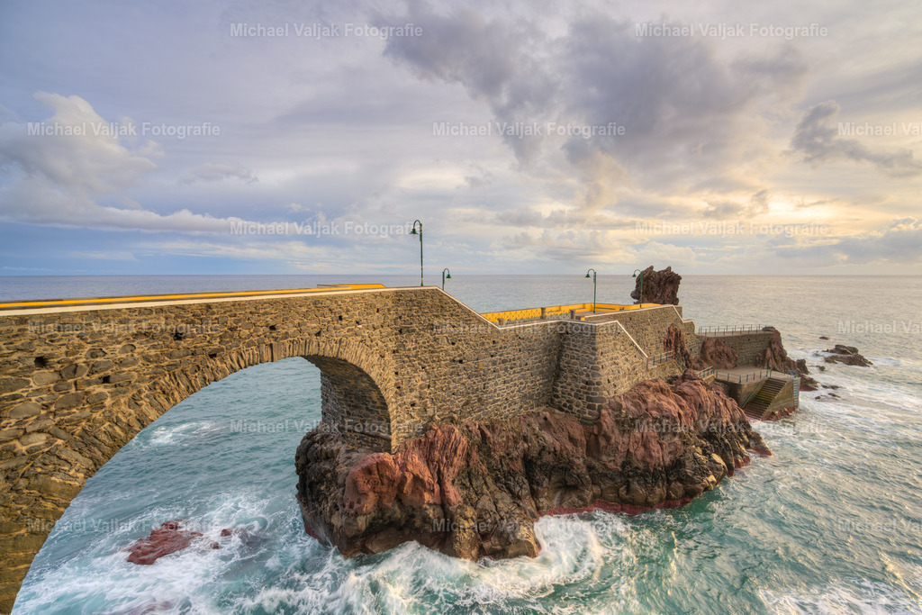 Ponta do Sol am Abend | Am Abend verwandelt sich die Steinbrücke in Ponta do Sol auf Madeira in ein romantisches Highlight. Die alten Steine leuchten im warmen Licht der untergehenden Sonne, und das sanfte Plätschern des Wassers darunter schafft eine beruhigende Kulisse. Ein Foto dieser Szene zeigt nicht nur die Brücke, sondern auch das Zusammenspiel von Natur und Architektur, das typisch für Madeira ist. Die reflektierenden Wasseroberflächen und das sanfte Abendlicht sorgen für ein Bild voller Harmonie und Frieden. - Realisiert mit Pictrs.com