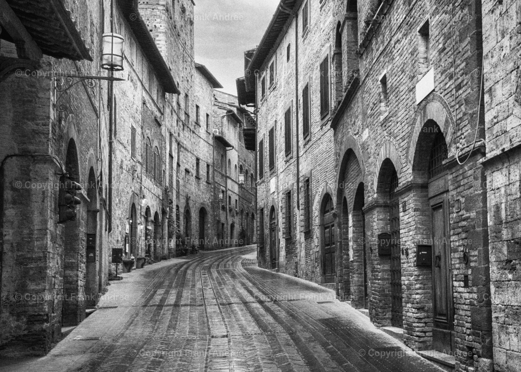 Altstadt von San Gimignano | Blick auf eine der zahlreichen historischen Straßen in der mittelalterlichen Altstadt von San Gimignano.
Stadtfotografie aus der Toskana in schwarz weiß. - Realisiert mit Pictrs.com