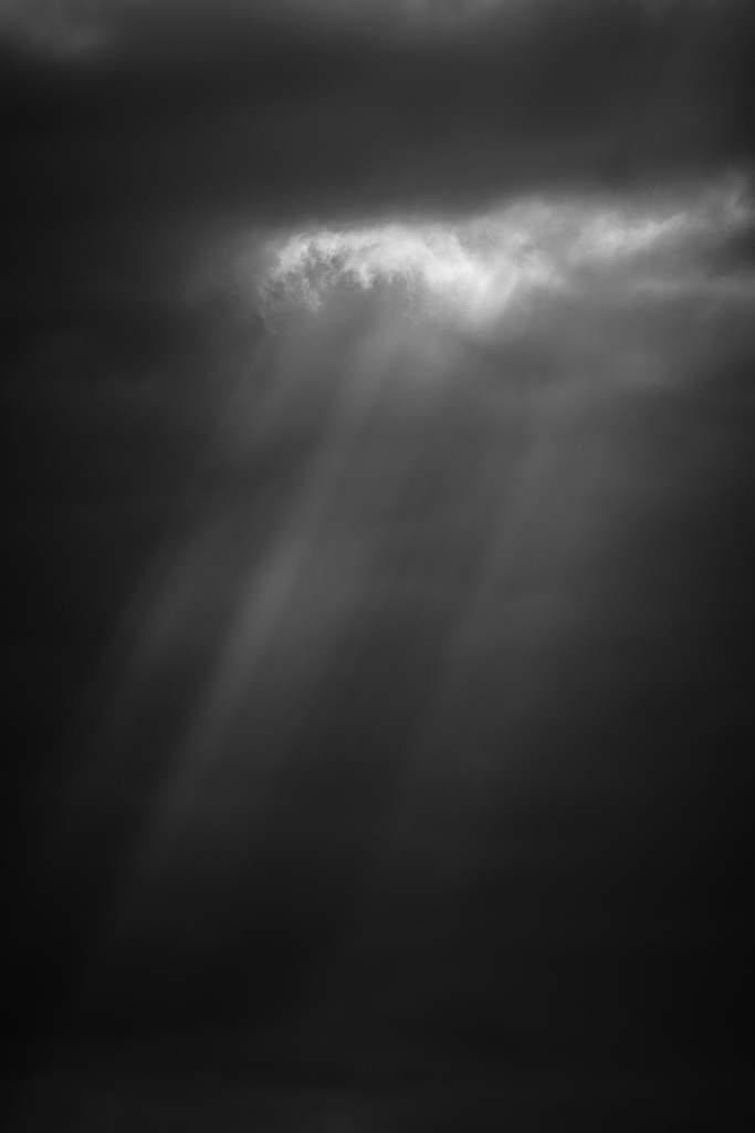 Hoffnung | Ein einzelner Lichtstrahl durchbricht die dunkle Wolkendecke und taucht den Himmel in eine eindrucksvolle Schwarzweißszene. Zwischen Schatten und Licht entsteht ein vergänglicher Moment, der Raum für eigene Gedanken lässt – ein Sinnbild für Zuversicht, selbst in den dunkelsten Augenblicken. - Realisiert mit Pictrs.com